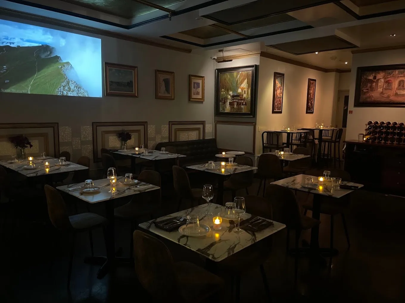 Candlelit marble tables across the dining room, a film playing on the far wall
